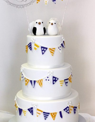 White wedding cake with yellow and purple bunting with birds
